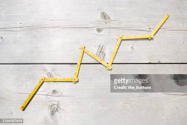 high angle view of a yellow folding ruler in shape of a stock curve on wooden background - rules stock pictures, royalty-free photos & images