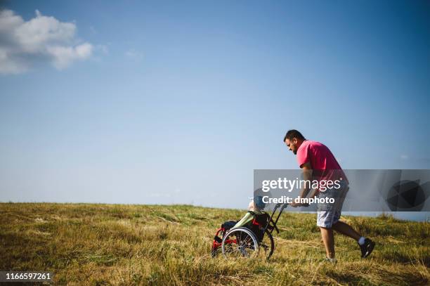 man pushing child in wheelchair - disabled child walker stock pictures, royalty-free photos & images