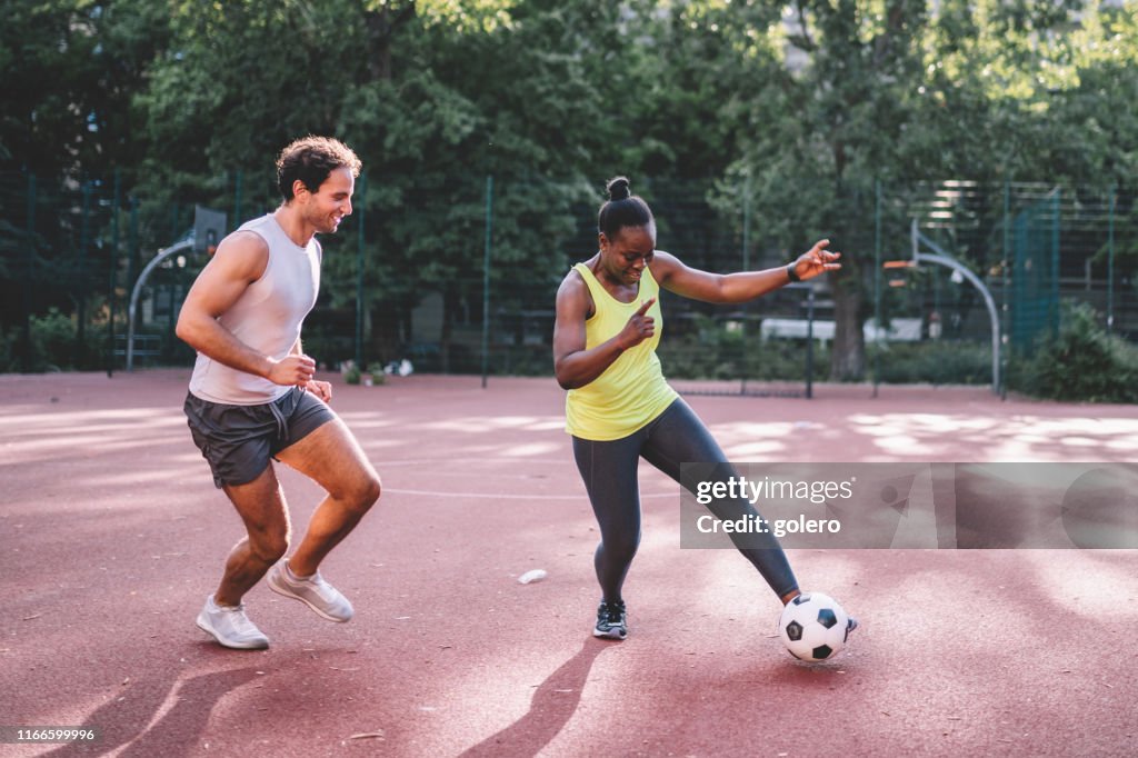 Young sportsman and woman playing soccer on hardcourt