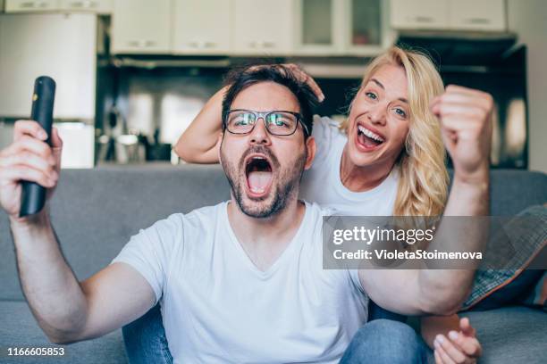 young couple watching sport on tv. - shouting match stock pictures, royalty-free photos & images