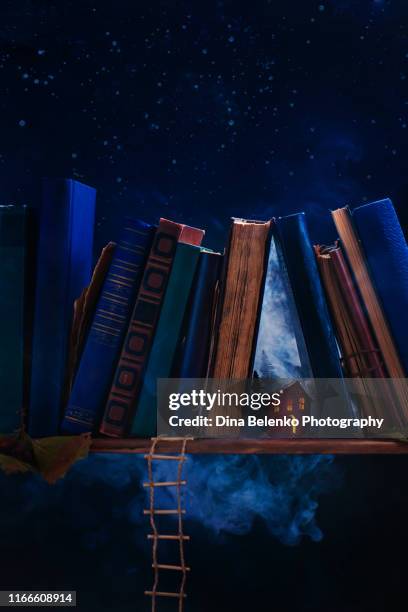 tiny paper house with light in windows on a book shelf. creative still life photography, tiny world metaphor. - legends classic stock-fotos und bilder