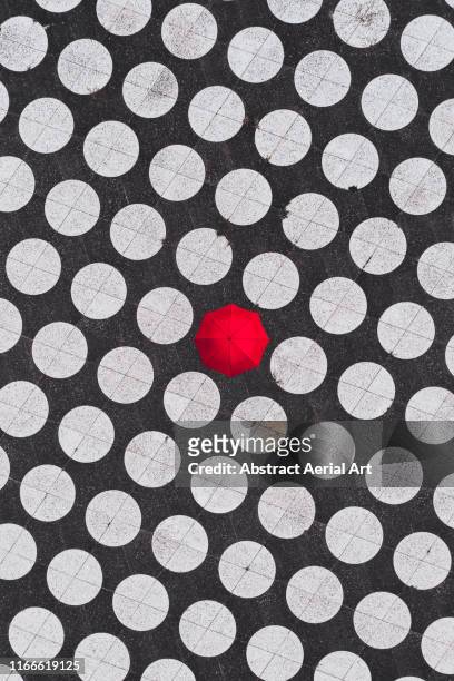 drone image directly above a person holding a red umbrella on a spotted floor surface, netherlands - red parasol stock pictures, royalty-free photos & images