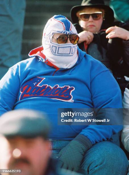 View of an unidentified New England Patriots fan, in a team hoodie, a ski mask , and sunglasses, as he sits in the stands, Foxboro, Massachusetts,...