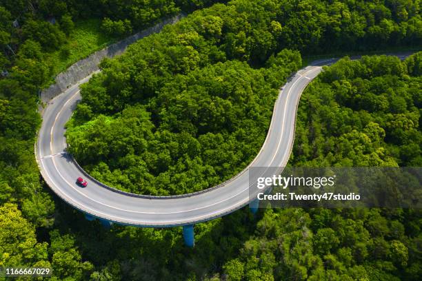 aerial view of curve road through green forest on mountain in summer - autoreifen natur stock-fotos und bilder