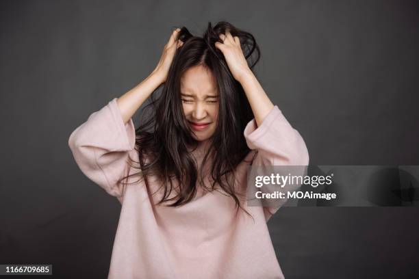 a young asian woman in a pink sweater is scratching her hair - psycho stockfoto's en -beelden