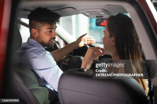 car merchant talking about new car model features to a young interested female buyer while sitting together in the display car in a dealership salon - sun visor stock pictures, royalty-free photos & images