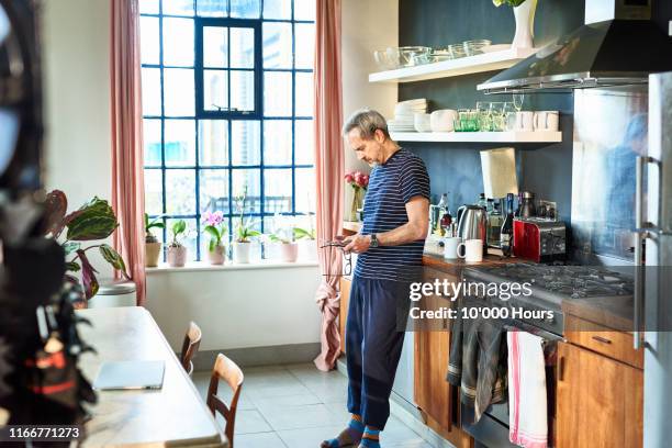 mature man using digital device at home in kitchen - autonomo smartphone tablet fotografías e imágenes de stock