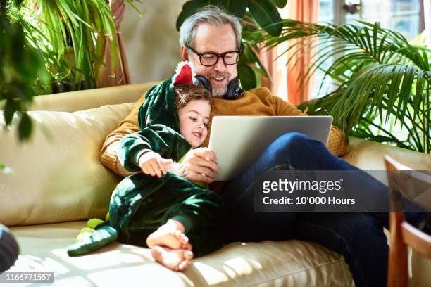 uncle playing game on laptop with girl in dinosaur outfit - family laptop stock pictures, royalty-free photos & images