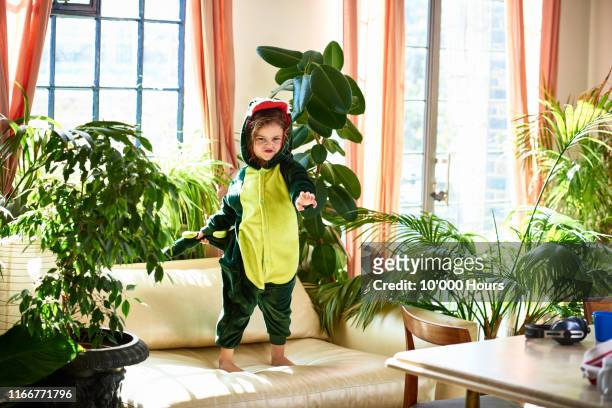 girl pretending to be dinosaur standing on sofa - acteren stockfoto's en -beelden