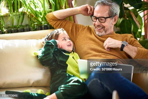 girl in dinosaur costume smiling at mature father on sofa - famille grands enfants photos et images de collection