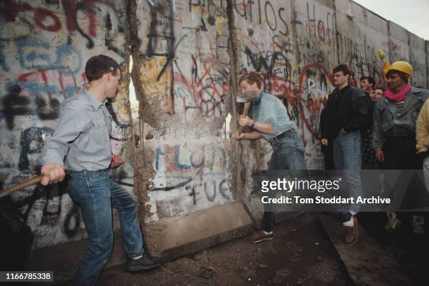 The first section of the Berlin Wall is torn down by crowds near the Brandenburg Gate on the morning of 10th November 1989. At centre, right is...