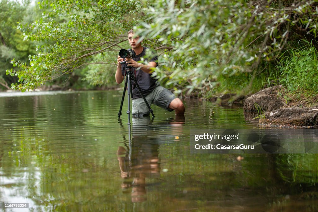Jonge fotograaf die een beeld van een ongemakkelijke positie in het midden van de rivier vastlegt