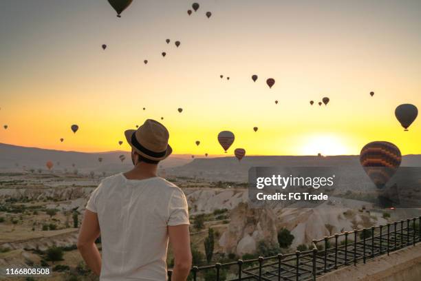 rear view of young adult man looking at balloons during sunset - festival de balonismo imagens e fotografias de stock