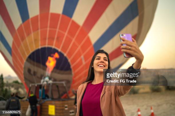 mulher nova que toma um selfie com um balão quente no fundo - balão de ar quente - fotografias e filmes do acervo