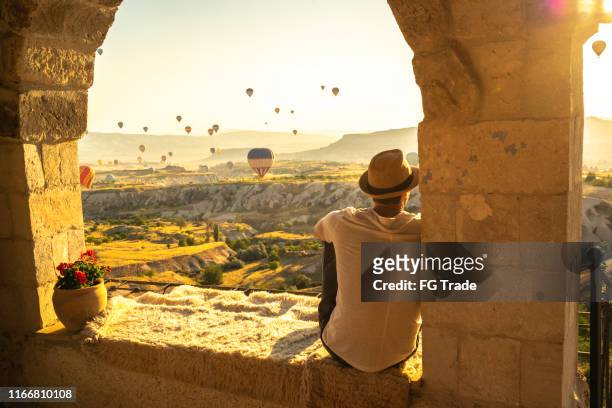 rear view of a young man sitting and looking at view during ballooning festival - cappadocia hot air balloon stock pictures, royalty-free photos & images