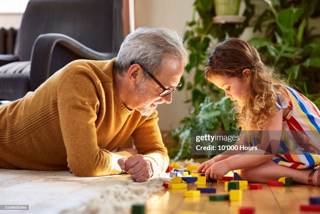 Granddaughter playing with wooden block and granddad watching