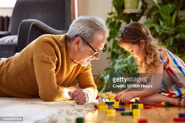 granddaughter playing with wooden block and granddad watching - pensioen thema stockfoto's en -beelden