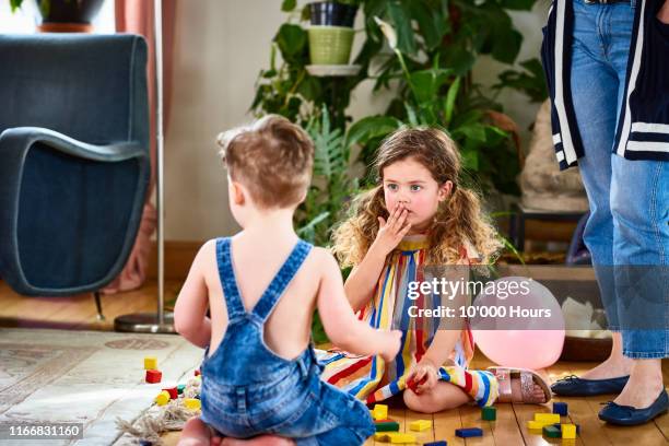 little girl with hand covering mouth sitting with brother - truth lies foto e immagini stock