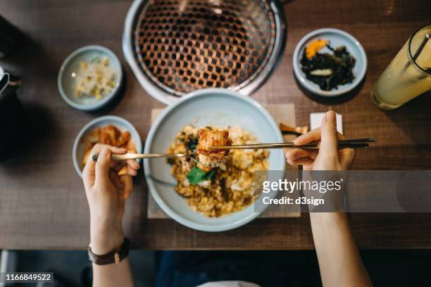 overhead view of woman eating korean style beef and scrambled egg rice bowl with kimchee in a korean restaurant - kimchee photos et images de collection