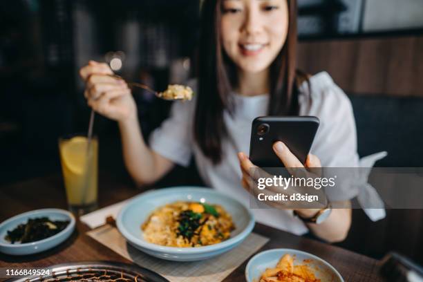 beautiful young woman looking at smartphone while having lunch in a restaurant - dinner program stock pictures, royalty-free photos & images