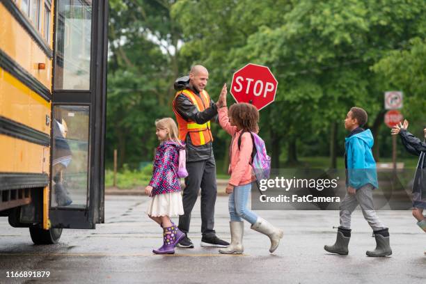 happy crossing guard gives children high fives as they board school bus - bus stop imagens e fotografias de stock