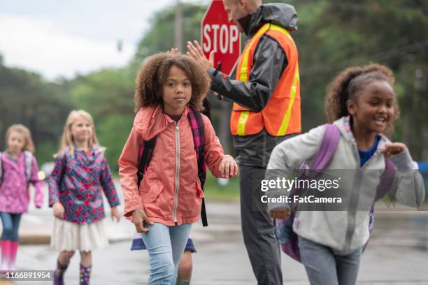 estudiantes de primaria cruzan la calle con la ayuda de cruzar guardia - vigilante de paso de peatones fotografías e imágenes de stock