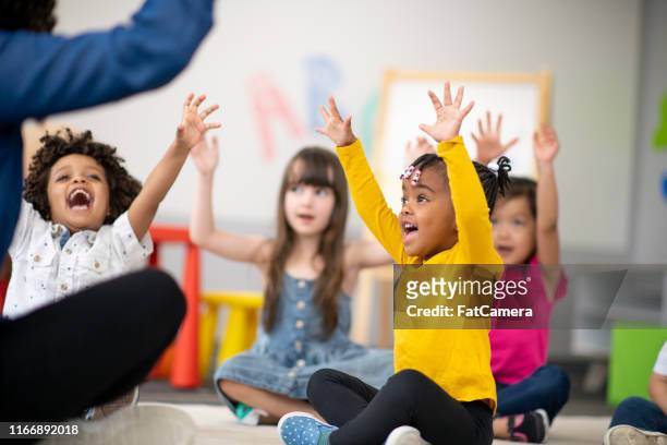 multi-ethnic group of preschool students in class - arms raised stock pictures, royalty-free photos & images