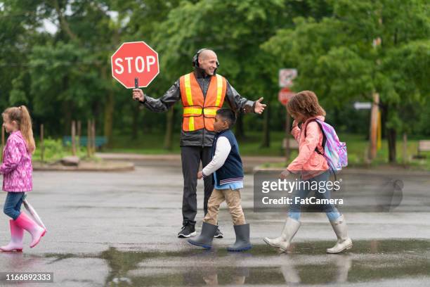 el protector de cruce sonriente ayuda a los estudiantes a cruzar la calle de forma segura - vigilante de paso de peatones fotografías e imágenes de stock