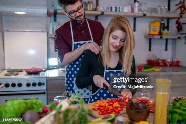 smiling young couple cooking food in the kitchen - loja de utensílios de cozinha imagens e fotografias de stock
