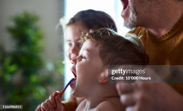 father showing son how to brush his teeth with mouth open - brothers bathroom stock-fotos und bilder