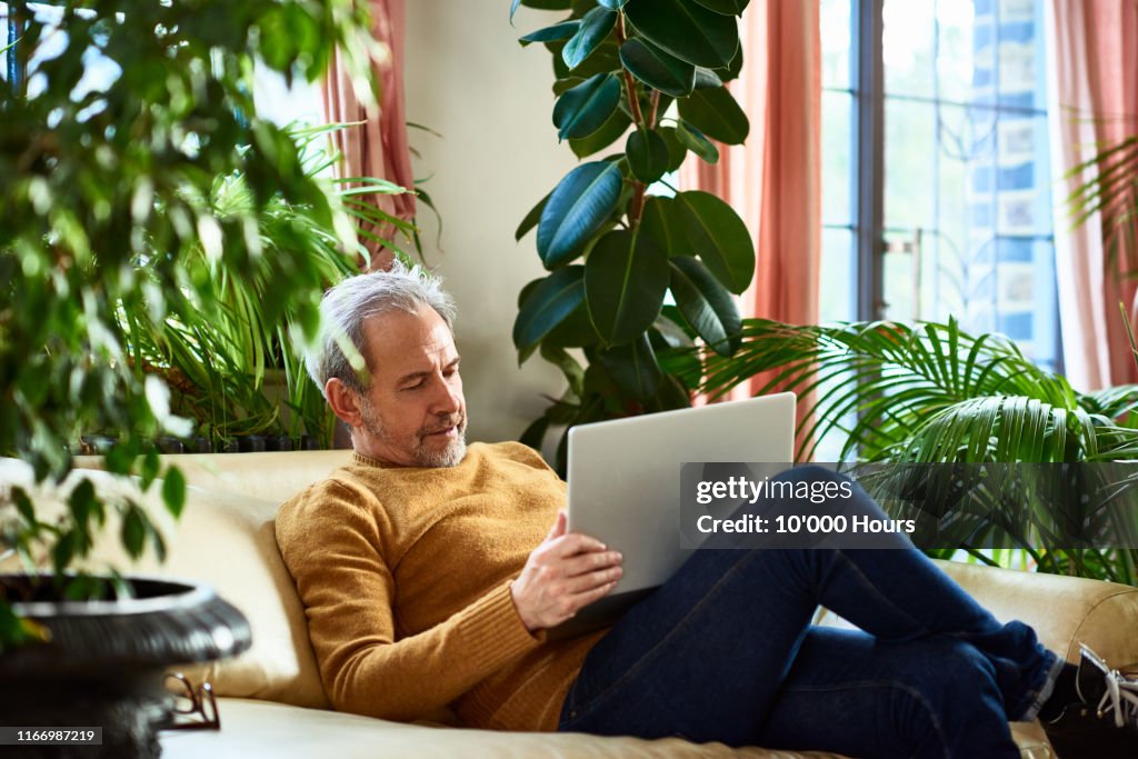Mature man using laptop on sofa at home