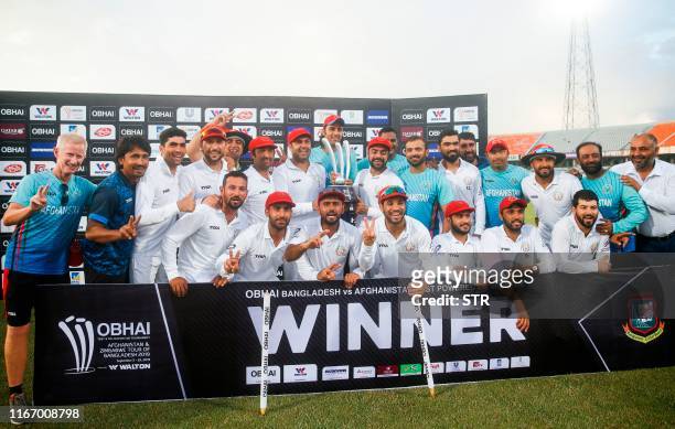 Afghanistan's cricketers and team members pose with their winning trophy after defeating Bangladesh in the one-off cricket Test match at Zohur Ahmed...