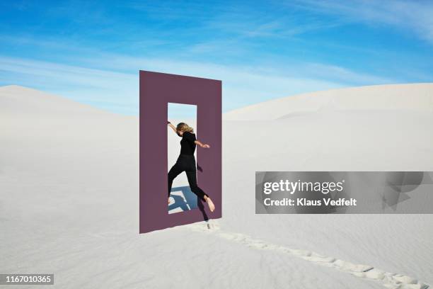 cheerful young woman jumping through door frame at desert - embrasure de porte photos et images de collection