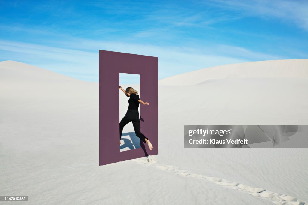 Cheerful young woman jumping through door frame at desert