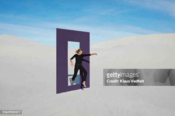 young woman jumping on white sand through door frame at desert - blank frame stockfoto's en -beelden