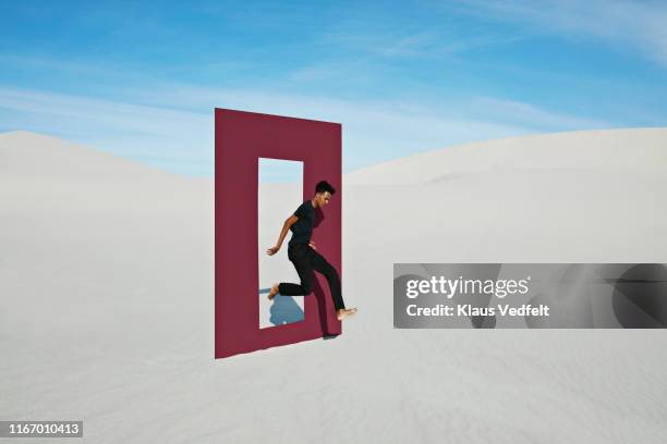 young man jumping on white sand through door frame at desert - walking side view stock-fotos und bilder