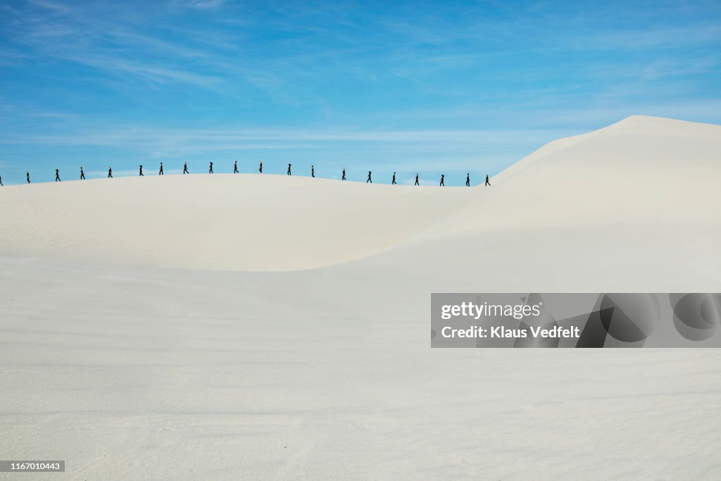 Distant multiple image of fashion models walking on sandy hill at desert