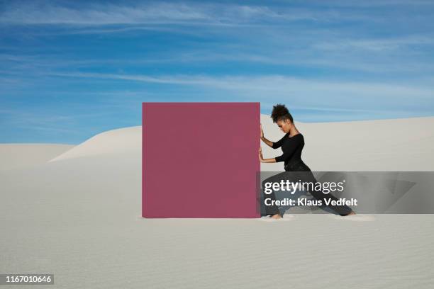 young woman pushing maroon portal on white sand dunes at desert - empujar fotografías e imágenes de stock