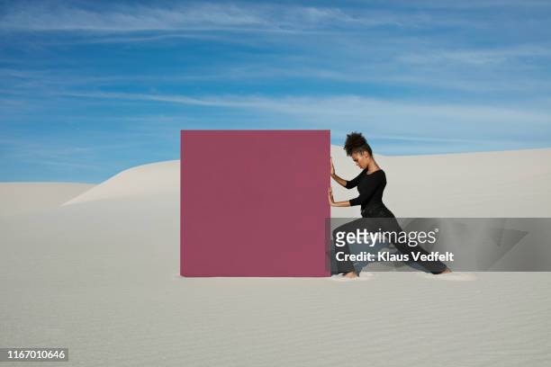 young woman pushing maroon portal on white sand dunes at desert - trying on ストックフォトと画像