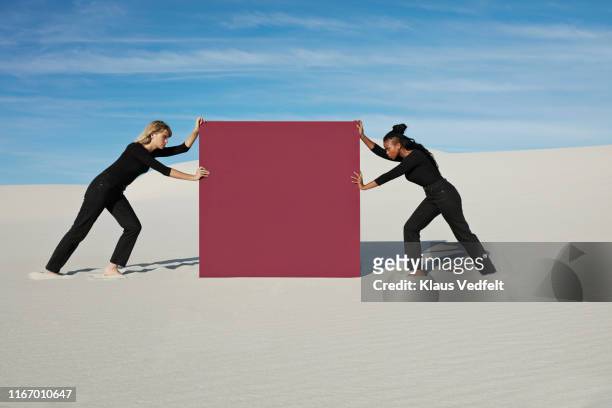 female models pushing maroon portal on white sand at desert - woman face off stock pictures, royalty-free photos & images