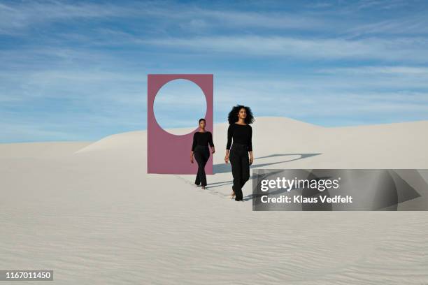 female models walking on white sand dunes against portal at desert - escapisme stockfoto's en -beelden