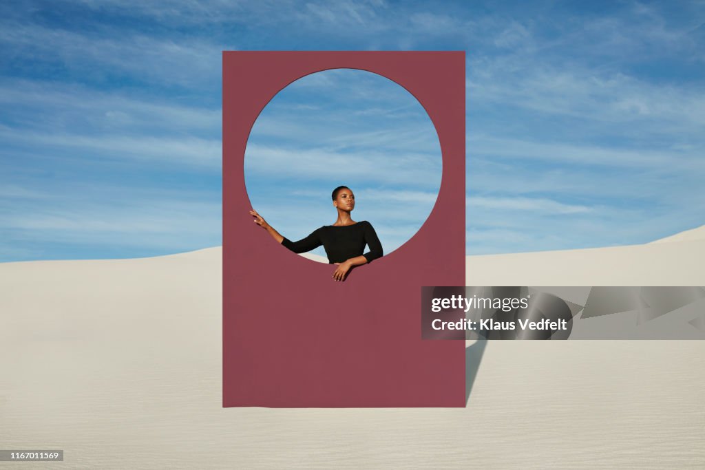 Young woman standing by window frame at white desert