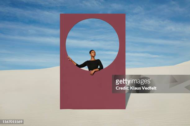 Young woman standing by window frame at white desert