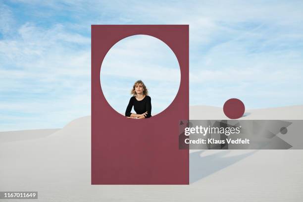 portrait of young woman standing by maroon portal at desert - leaning stockfoto's en -beelden
