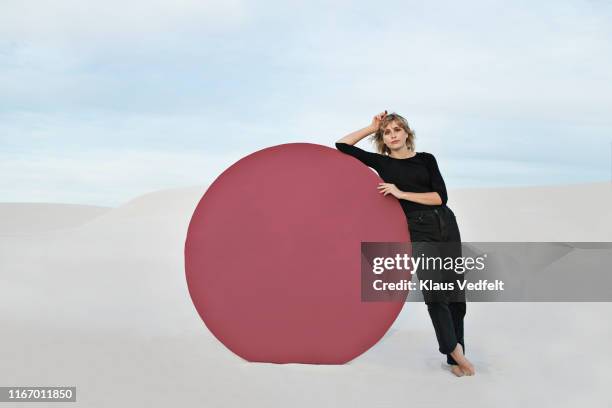 portrait of young woman standing by circular portal at desert - leaning stock-fotos und bilder