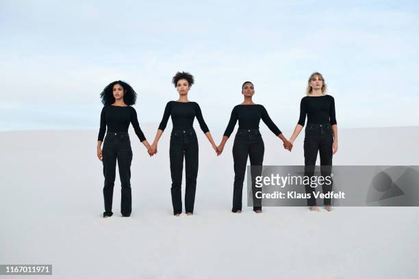 young female models holding hands while walking at desert during sunset - nur erwachsene stock-fotos und bilder