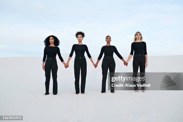 young female models holding hands while walking at desert during sunset - black trousers fotografías e imágenes de stock