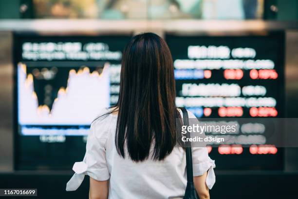 Rear view of businesswoman looking at stock exchange market display screen board in downtown financial district