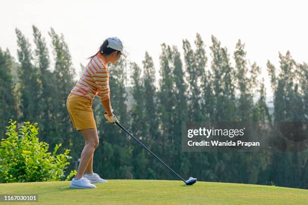 healthy sport. asian sporty woman golfer player doing golf swing tee off on the green evening time, she presumably does exercise. healthy lifestyle concept - golf swing sunset stock pictures, royalty-free photos & images