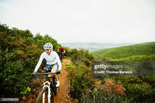 mature woman climbing hill while riding mountain bike on trail with husband - california strong stockfoto's en -beelden